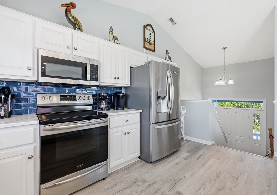 Step into your fully equipped kitchen where cooking becomes a pleasure. Crisp white cabinetry, modern stainless steel appliances, and a charming blue tile backsplash create a bright, welcoming space for preparing your favorite vacation meals.