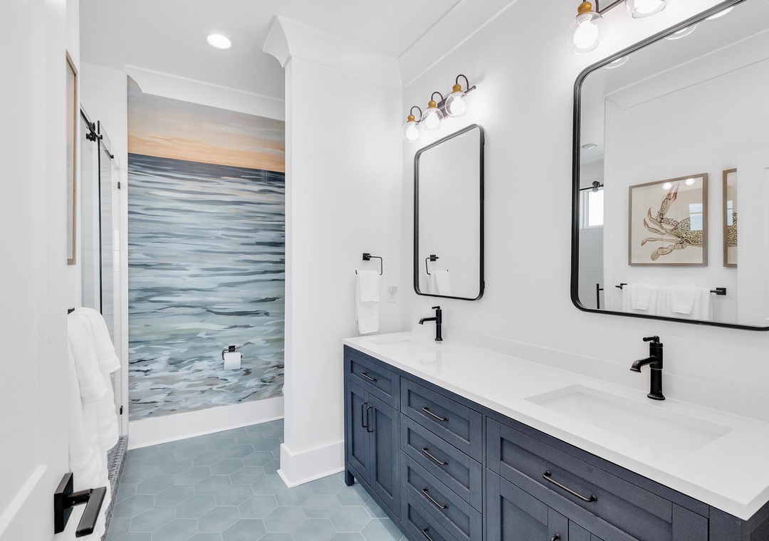 Freshen up in this serene coastal-inspired bathroom with dual sinks, elegant black fixtures, and a beautifully tiled shower that brings the ocean right to your doorstep.