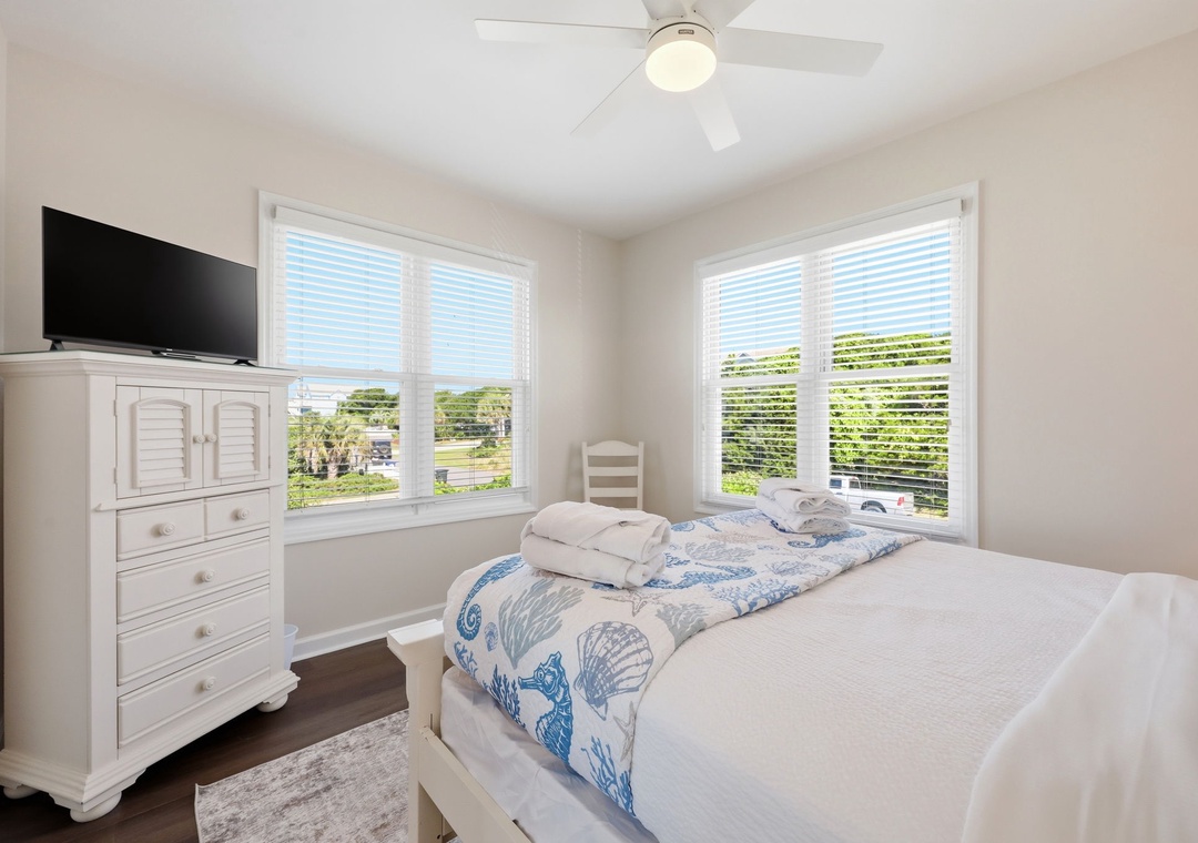 Settle into this serene bedroom where natural light frames peaceful views of the surrounding landscape. Your coastal retreat awaits with crisp linens, thoughtful beach-inspired touches, and a gentle ceiling fan overhead.