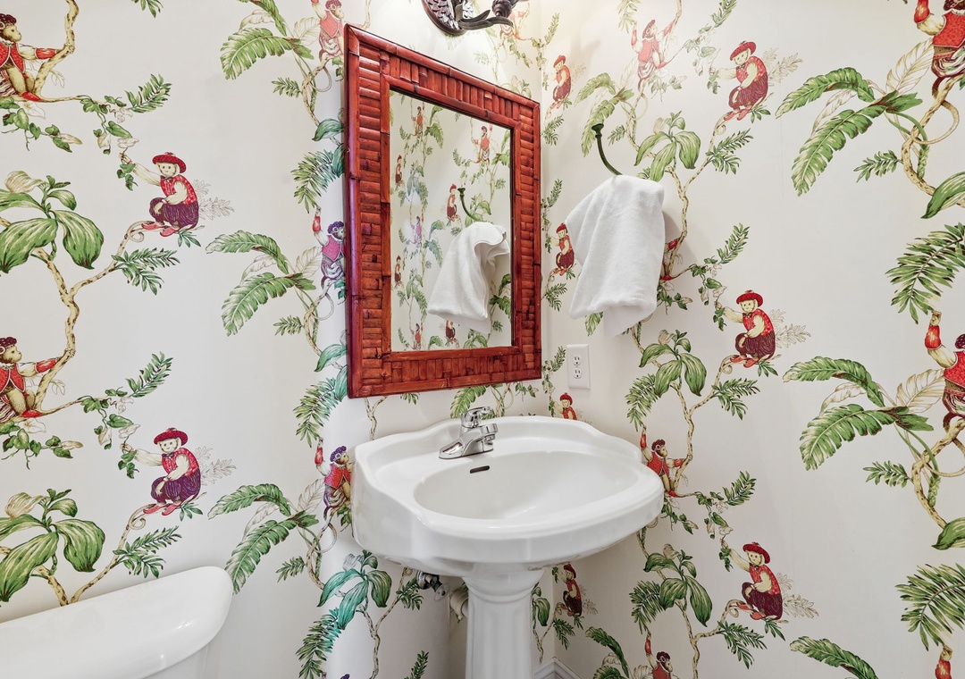 Freshen up in this whimsical bathroom adorned with playful tropical wallpaper. The classic pedestal sink and bamboo-framed mirror add a charming, cottage-style touch to your stay.
