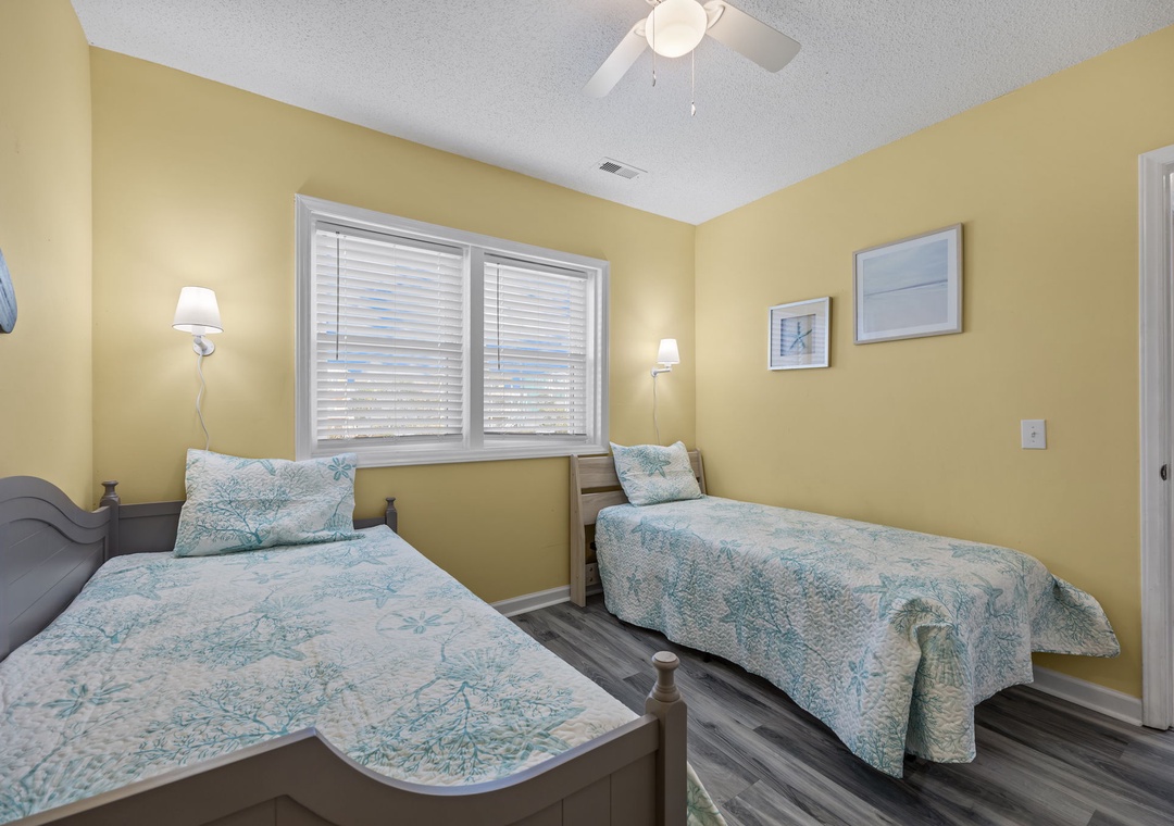 Twin beds dressed in coastal-inspired linens create the perfect spot for restful sleep beneath warm yellow walls and gentle ceiling fan breezes.