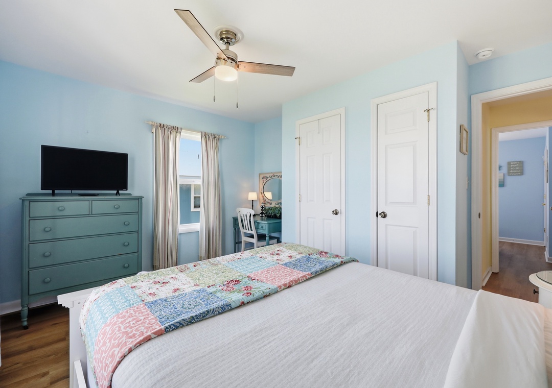 Picture yourself waking up in this serene coastal-inspired bedroom. Soft blue walls and a gentle ceiling fan create a refreshing retreat, while your flatscreen TV awaits your favorite shows after exploring.