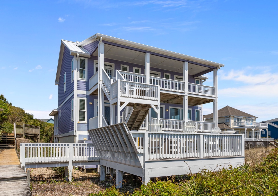 Charming coastal home with wraparound balconies and ocean access, nestled among neighboring beach houses under clear blue skies.