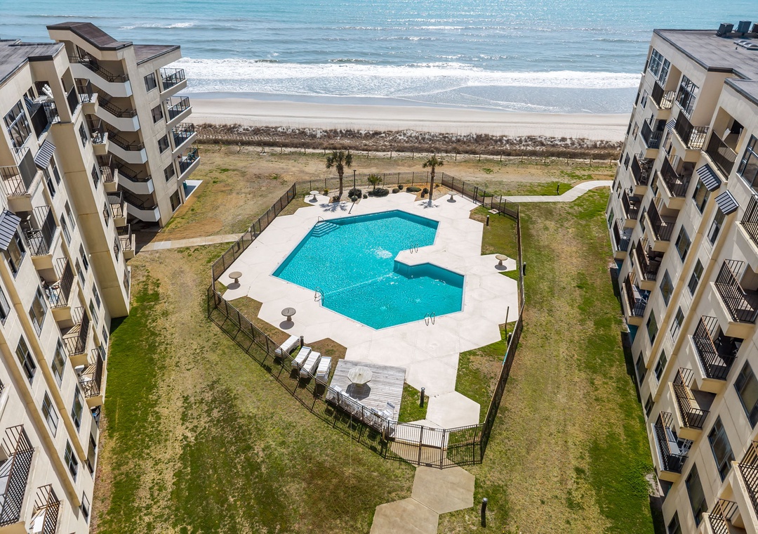 Beachfront property with direct access to sandy shores, featuring a sparkling pool nestled between multi-story buildings with private balconies overlooking the ocean.