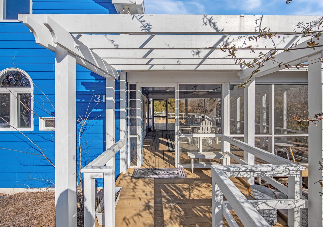 Charming blue cottage entrance with white pergola-covered deck creates your perfect coastal retreat arrival experience.