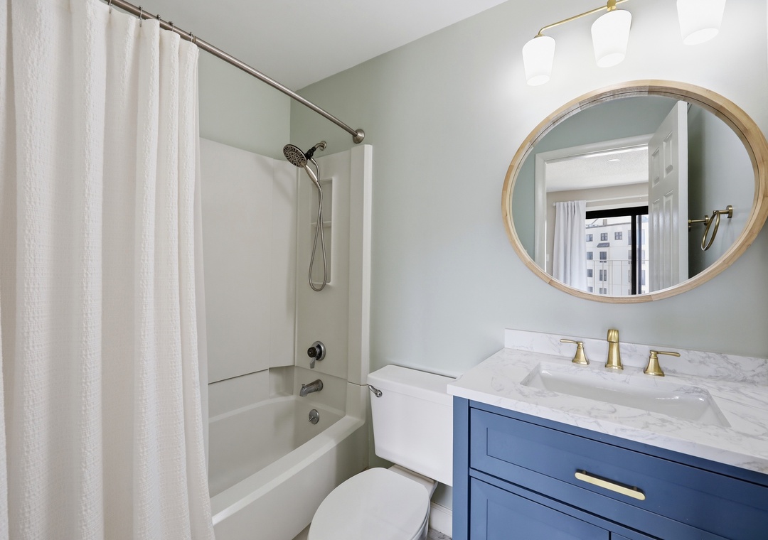 Step into a beautifully refreshed bathroom featuring soft coastal hues, a spacious tub-shower combo, elegant marble vanity, and warm lighting to start your day right.