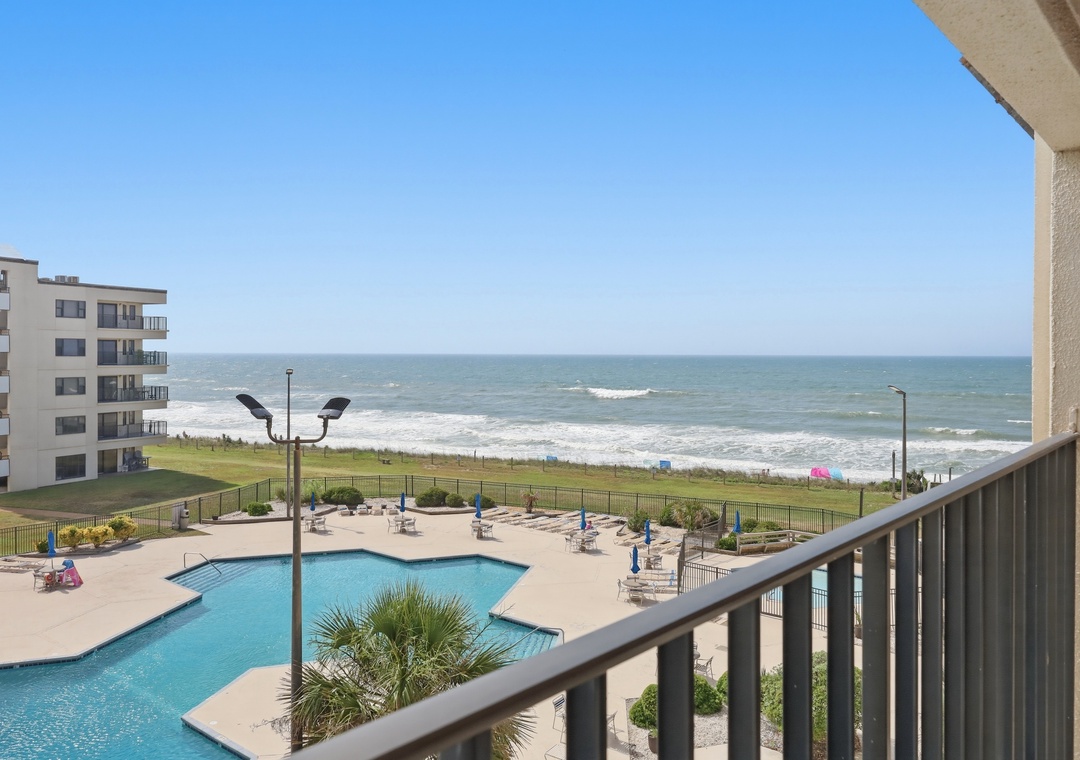 Beachfront property offers direct ocean access, an outdoor pool, and coastal resort ambiance with adjacent buildings and green lawn areas.