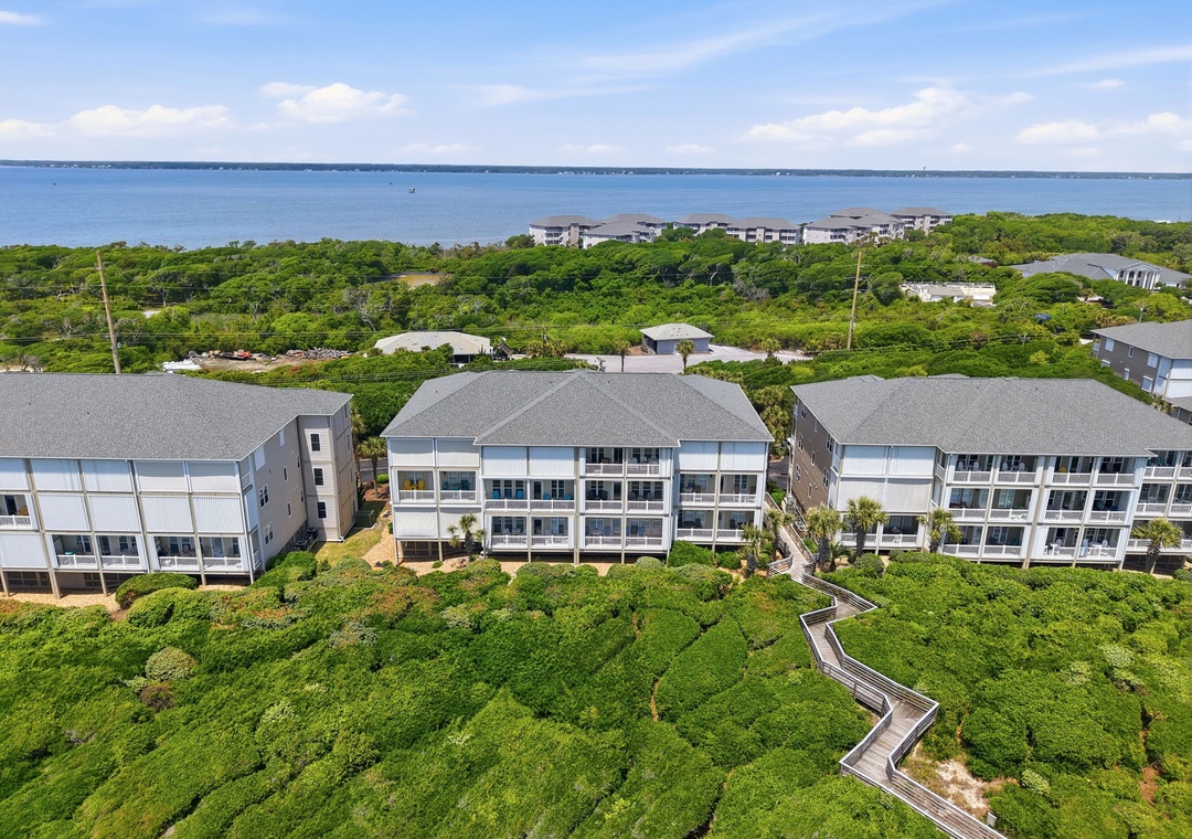 Beachfront vacation community nestled among lush coastal greenery with boardwalk access, ocean views, and nearby islands dotting the horizon.