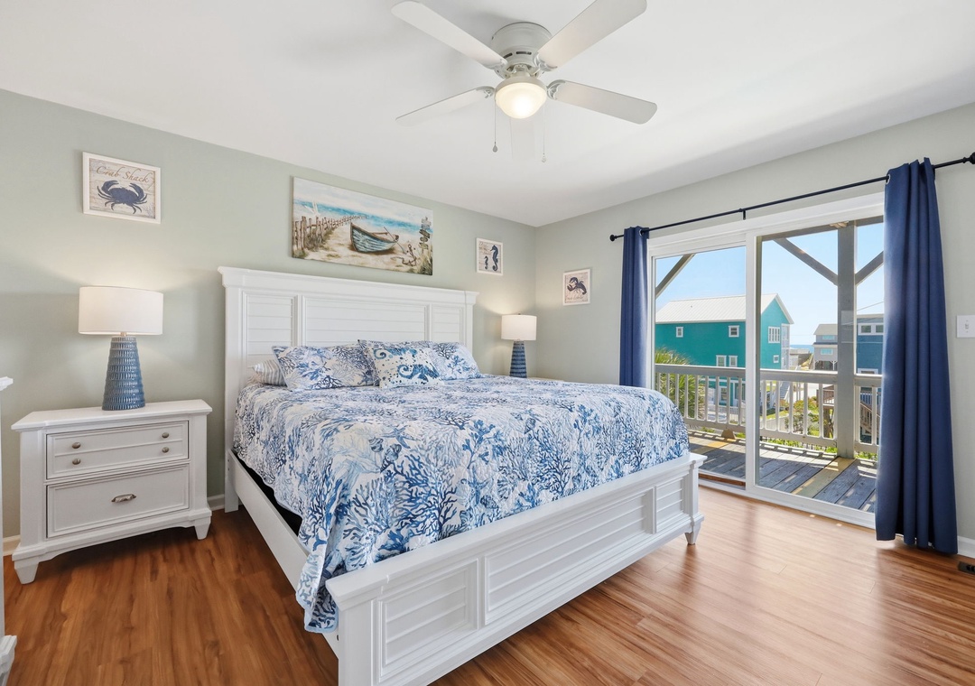 Wake up to bright coastal views and ocean breezes in this serene bedroom. Plush bedding, warm wood floors, and a private balcony overlooking colorful beach homes make mornings here unforgettable.