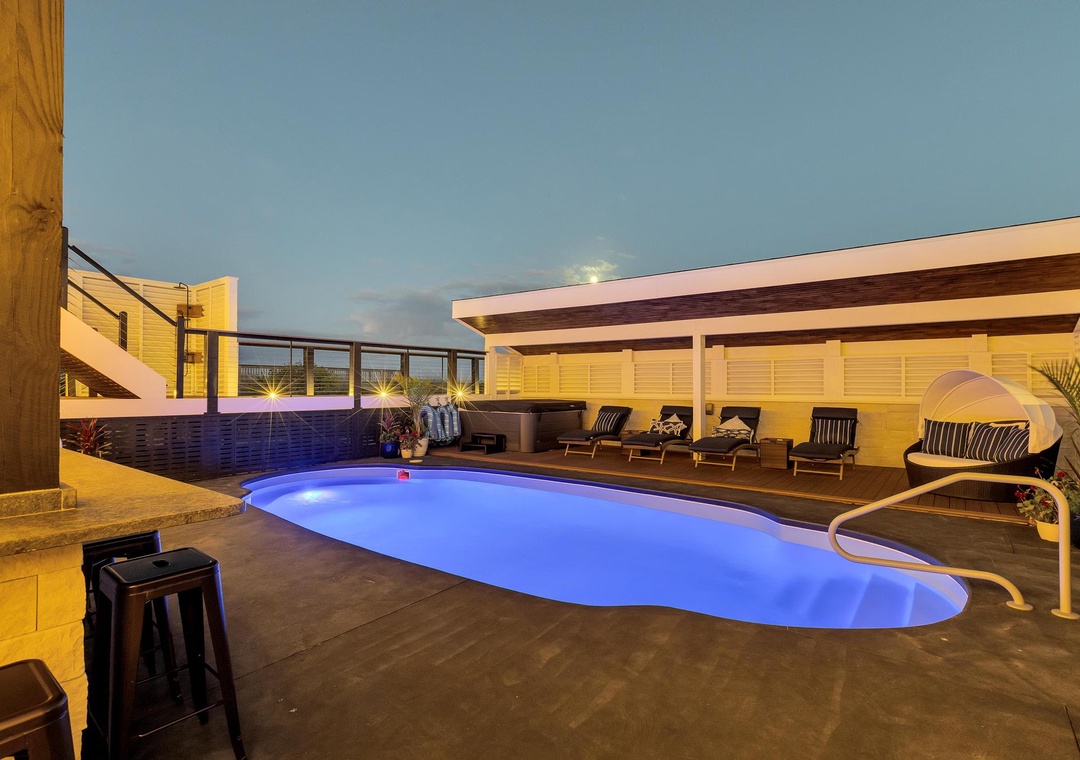 Modern vacation rental with illuminated pool, lounge seating, and a covered pavilion capturing golden-hour glow beneath a serene evening sky.