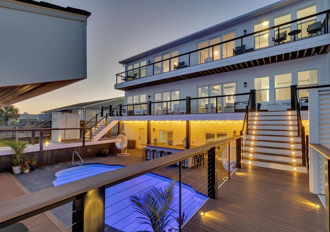 Modern beachside property featuring multi-level decks, an inviting pool, and stylish outdoor entertaining spaces illuminated at dusk.