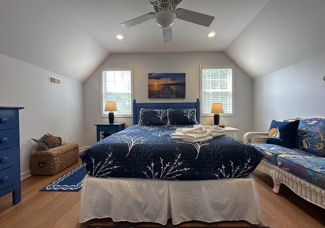 Sink into soft coastal linens and wake to natural light streaming through dual windows. The vaulted ceiling and ceiling fan keep your sanctuary fresh and airy.