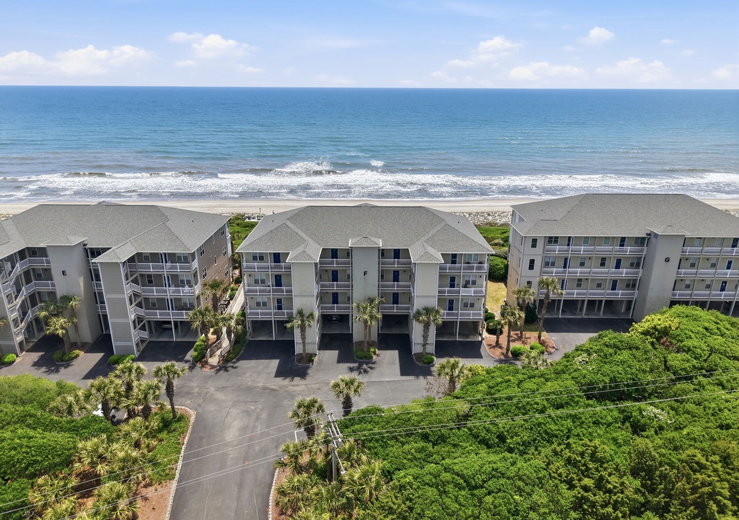 Aerial view of beachfront vacation rental buildings positioned directly along a pristine coastline, featuring tropical landscaping and convenient parking areas near the entrance.