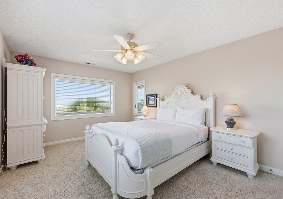 Sink into crisp white linens under soft ceiling fan light. Your elegant white bedroom offers peaceful views and ample storage for a restful coastal retreat.