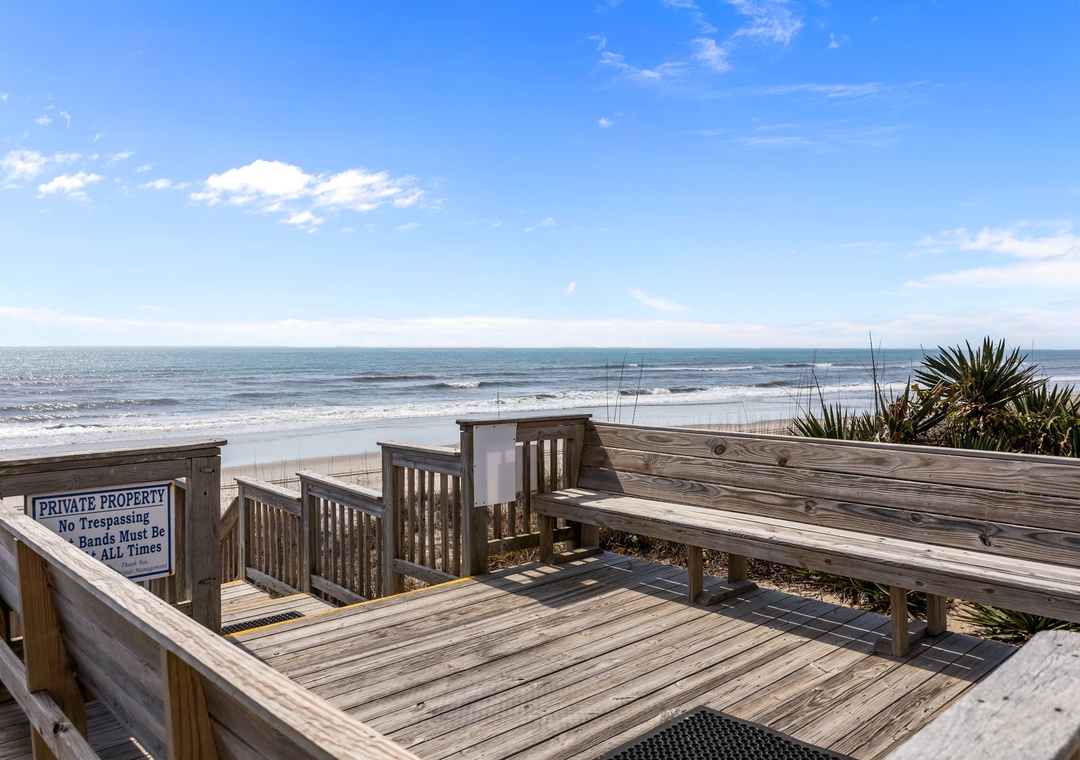 Private beach access with wooden deck and stairs leading directly to sandy shores and rolling waves, offering exclusive coastal retreat surroundings.
