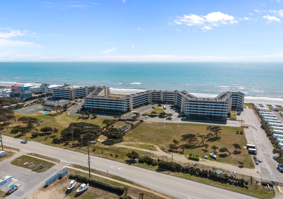 Beachfront property complex situated along pristine coastline with direct access to sandy shores and turquoise waters, surrounded by green spaces and coastal parkland.