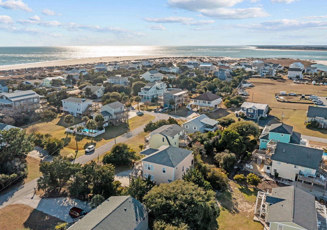 Aerial view of a coastal community featuring beach houses nestled among trees, with pristine sandy beaches and ocean views nearby.
