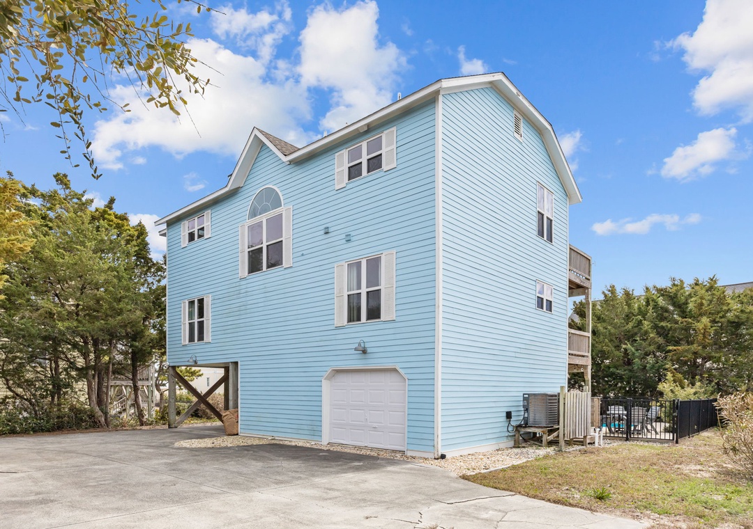 Charming blue beach house with elevated design, garage parking, and mature landscaping creates the perfect coastal retreat setting.