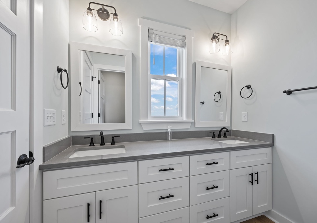 Your spacious dual-vanity bathroom features gleaming quartz countertops and crisp white cabinetry, perfectly lit for your morning routine.