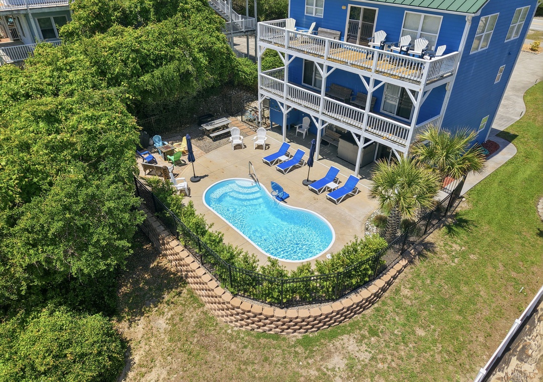 Aerial view of the vibrant blue property featuring a private kidney-shaped pool surrounded by sunbeds and lush greenery, perfect for a coastal getaway.