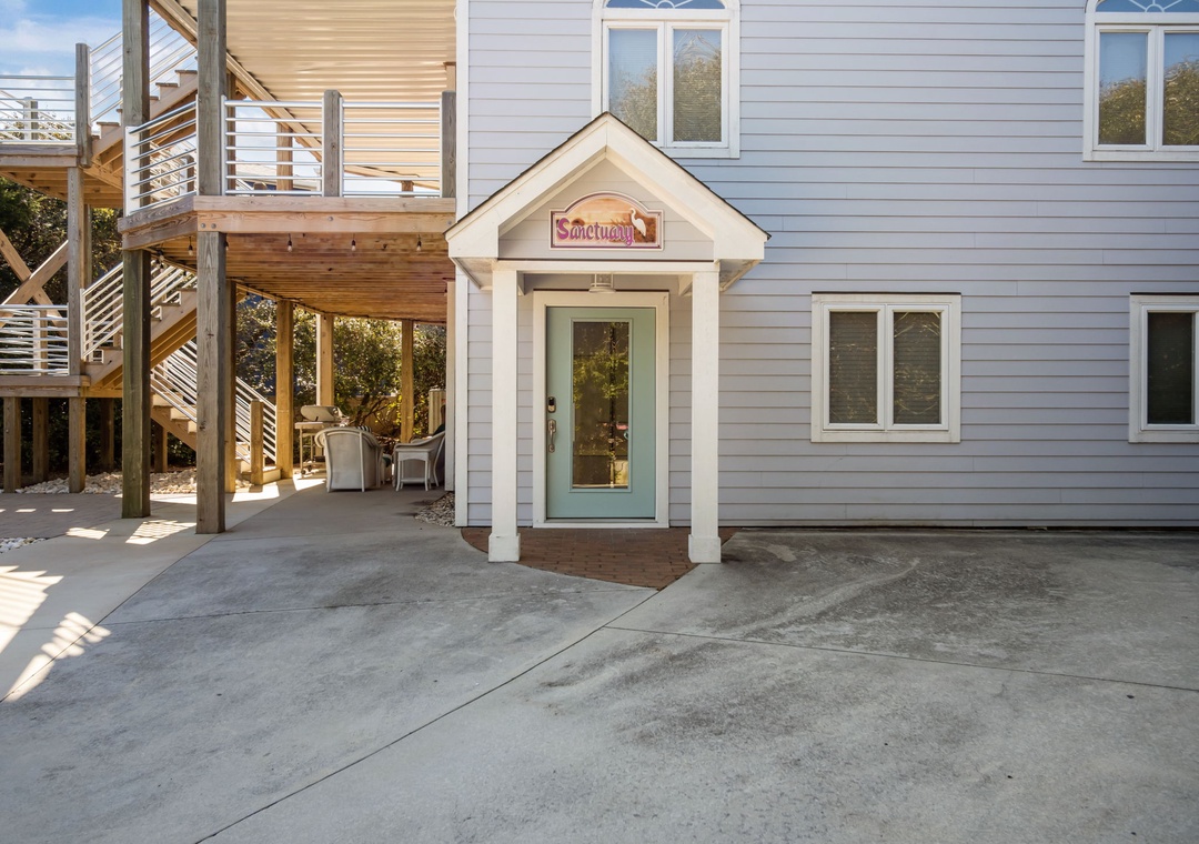 The welcoming entrance to Sanctuary, featuring charming coastal architecture with wooden decking, outdoor seating area, and contemporary design elements.