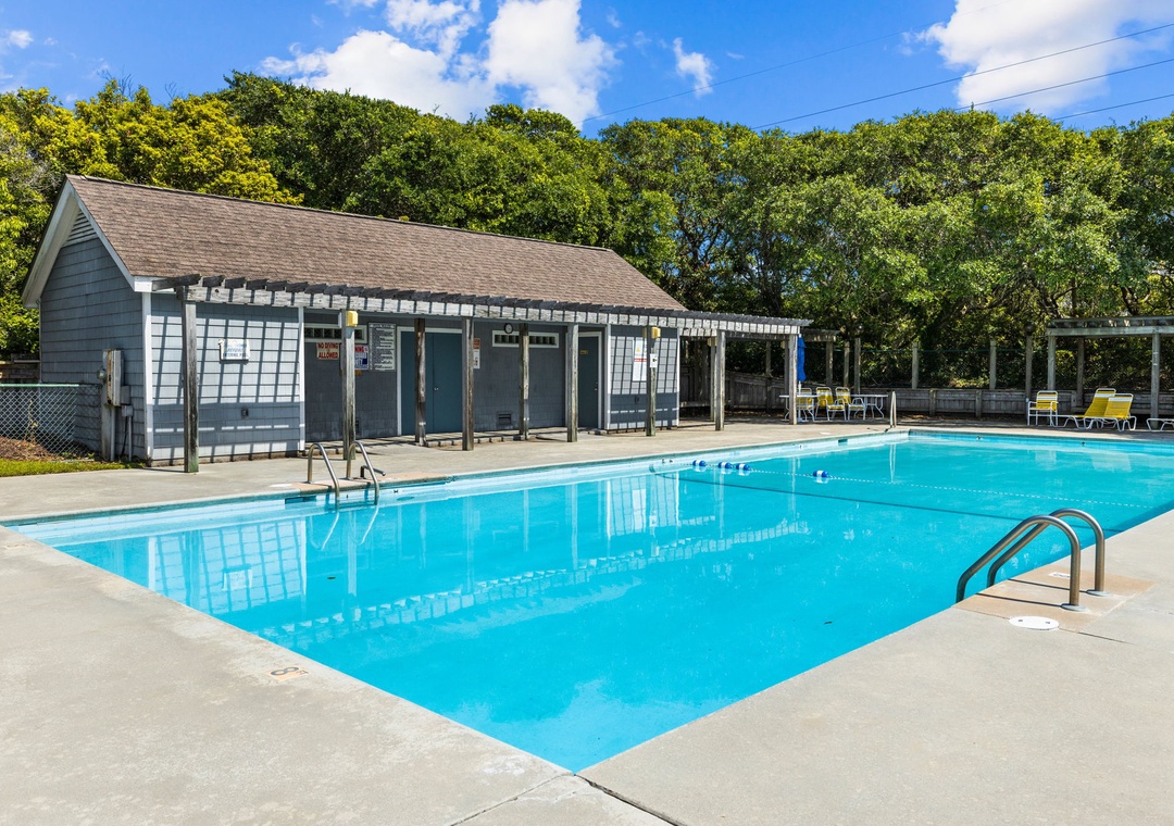 Community swimming pool with poolside building and changing facilities surrounded by lush greenery.