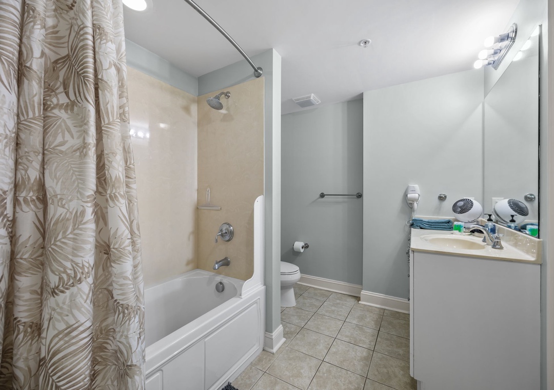 Step into your peaceful bathroom retreat featuring a relaxing tub-shower combo, modern vanity, and tropical-patterned curtains for your comfort.