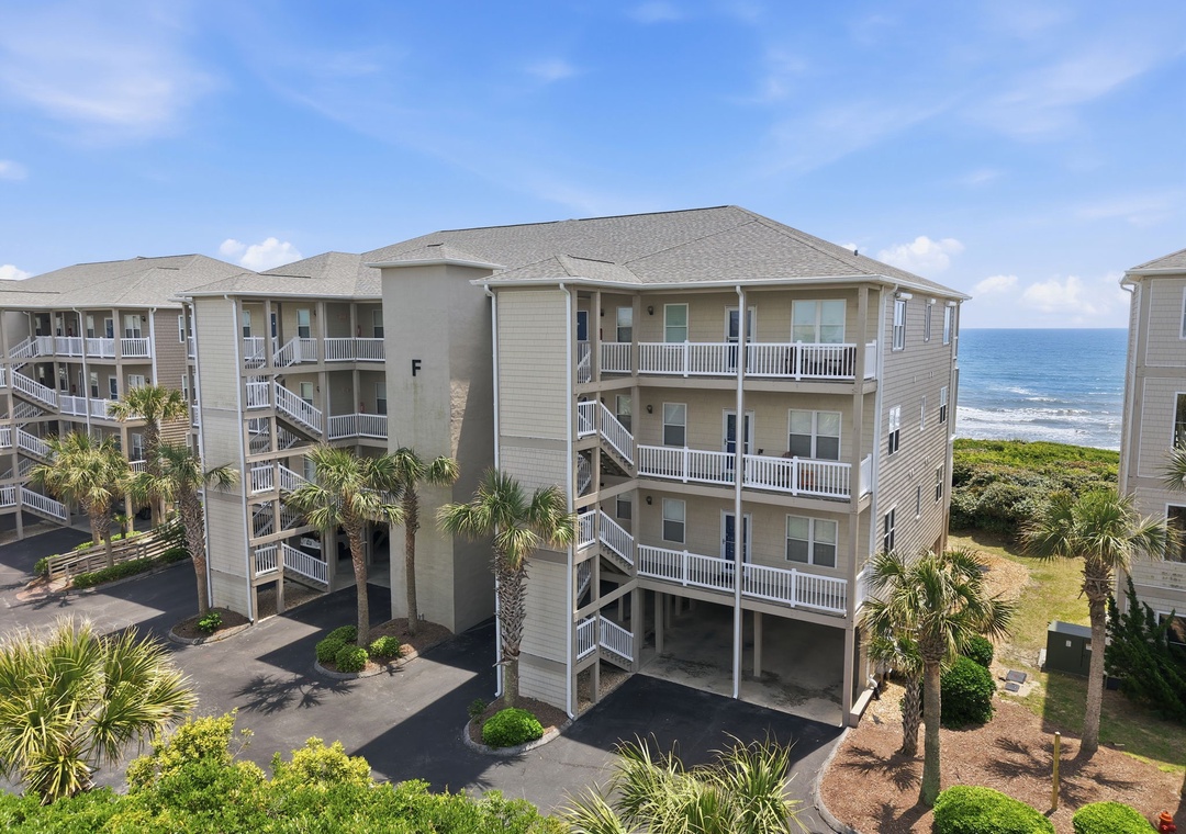 Coastal vacation property featuring multi-level balconies with direct ocean views, surrounded by tropical palm trees and manicured landscaping. The beachfront complex offers immediate access to sandy shores.