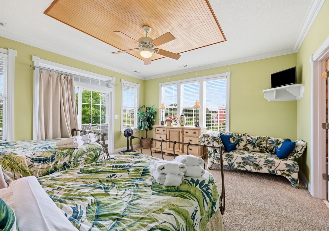 Your tropical-inspired retreat features two plush beds and a cozy seating area, where natural light streams through multiple windows. Drift to sleep under the warm glow of the ceiling fan, surrounded by lush palm-printed linens.