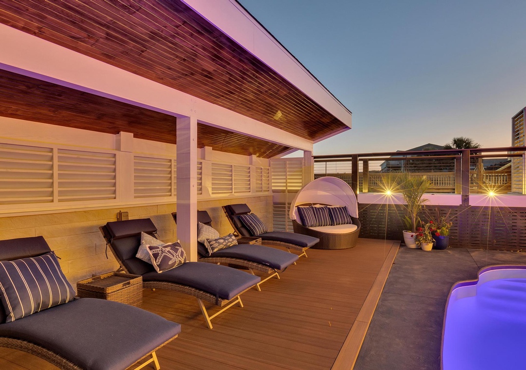 Modern rooftop deck featuring lounge chairs, a daybed, and ambient lighting—perfect for relaxing under the evening sky after a day of exploration.