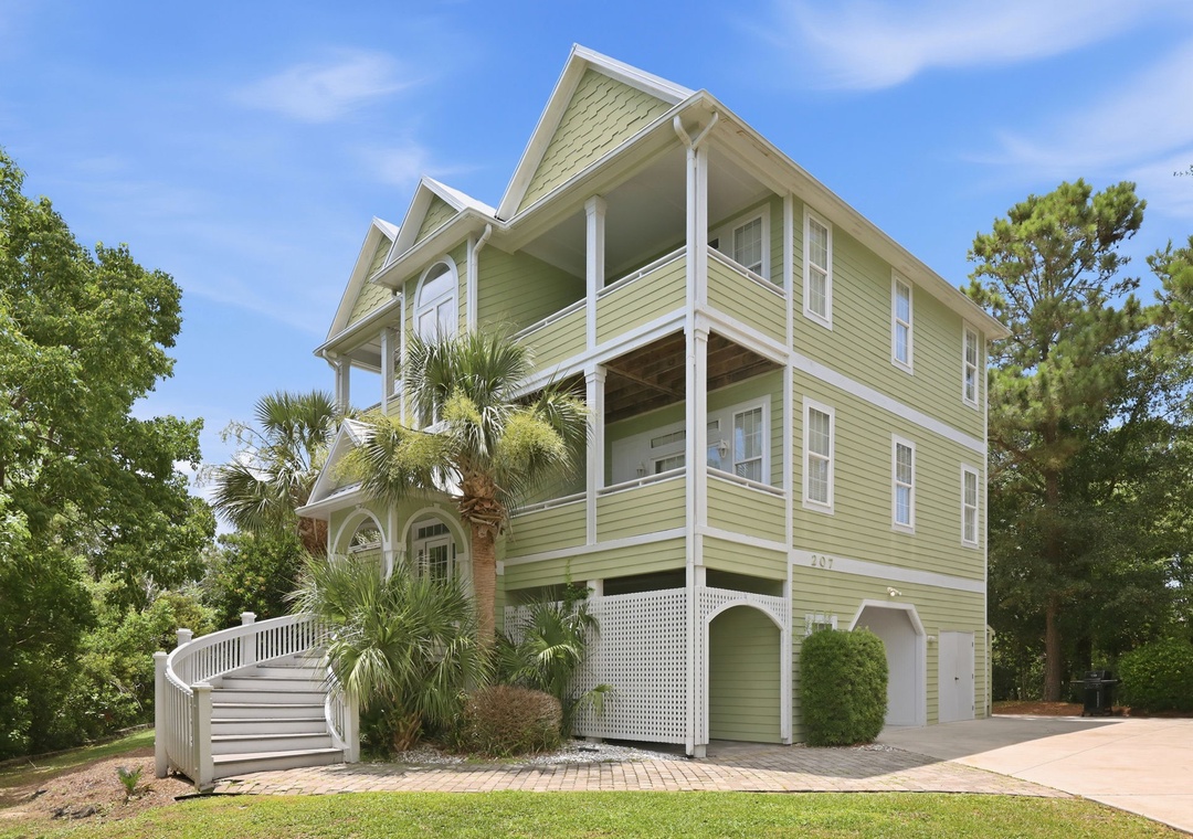 This charming coastal-style property sits nestled among lush trees and tropical palms, offering a private entrance and a welcoming staircase that leads to beautifully appointed living spaces throughout multiple levels.