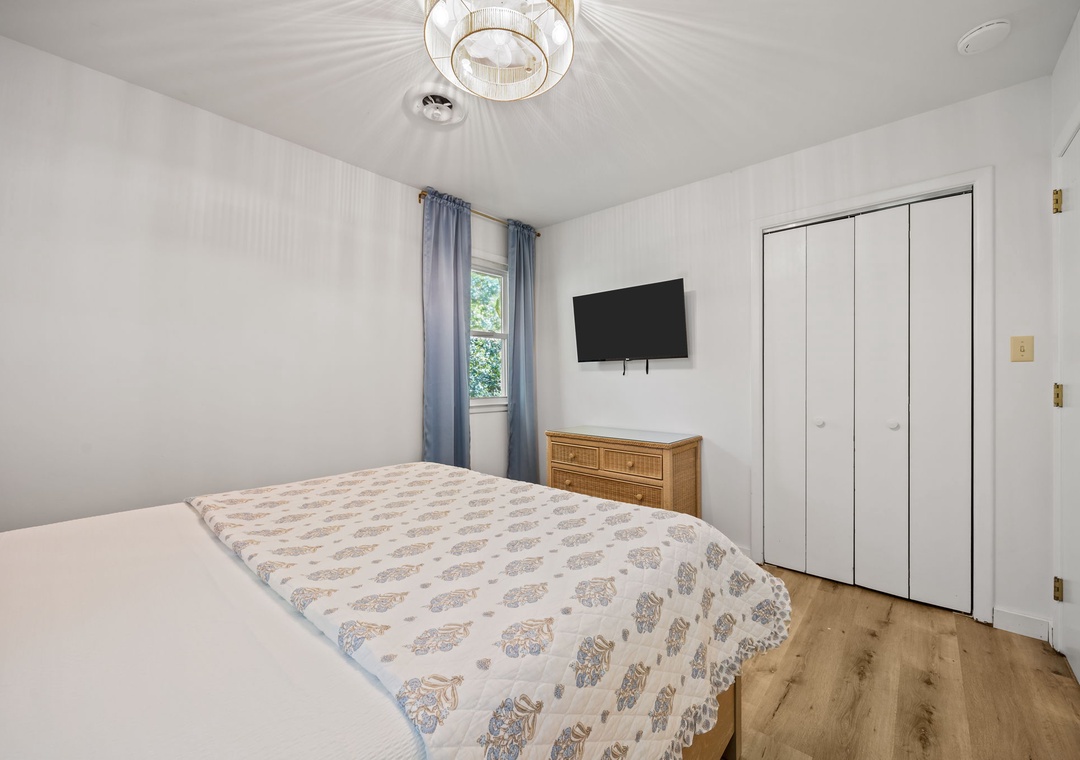 Unwind in your peaceful bedroom featuring a comfortable bed, modern TV, and elegant chandelier for the perfect night's rest.