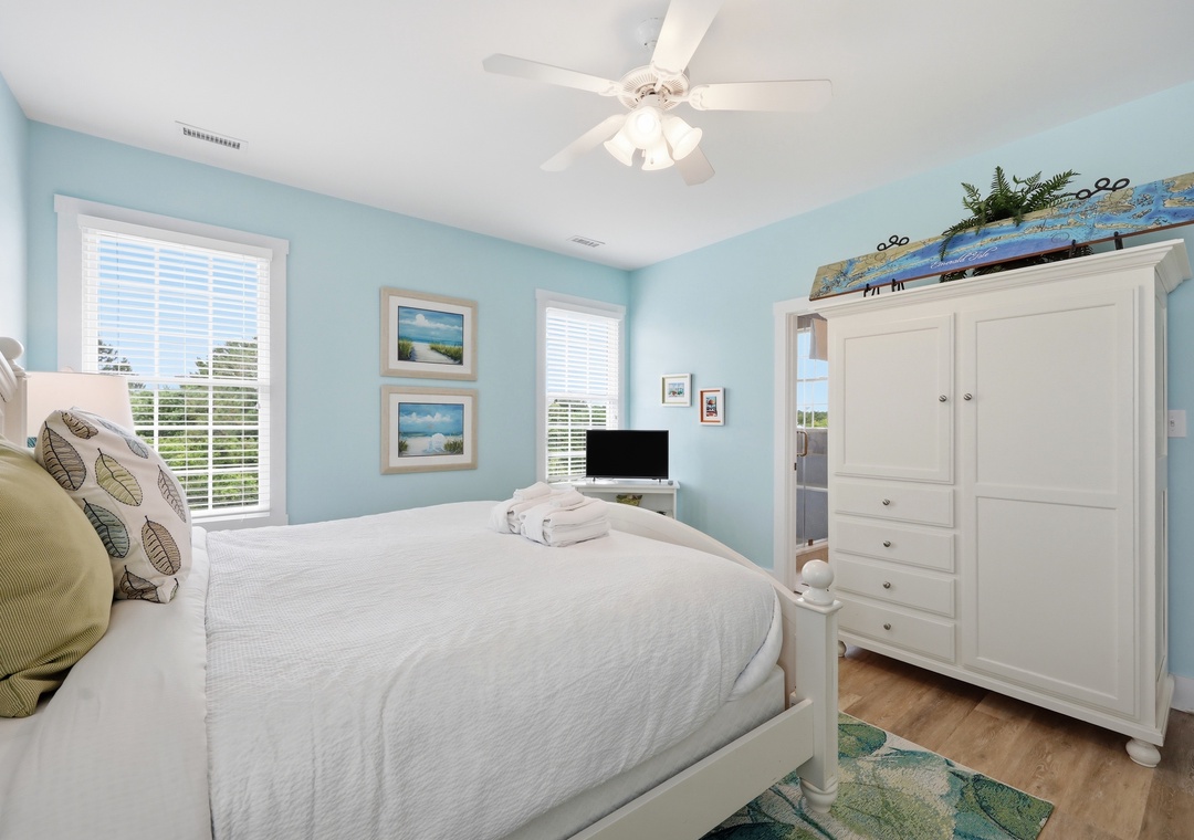 Drift off in your coastal-themed bedroom, where soft blue walls and crisp linens create a serene retreat. Natural light pours through the windows, while the ceiling fan keeps you cool and comfortable.