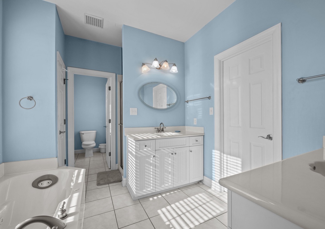 Freshen up in your spacious bathroom featuring serene blue walls, bright vanity lighting, and a relaxing soaking tub.