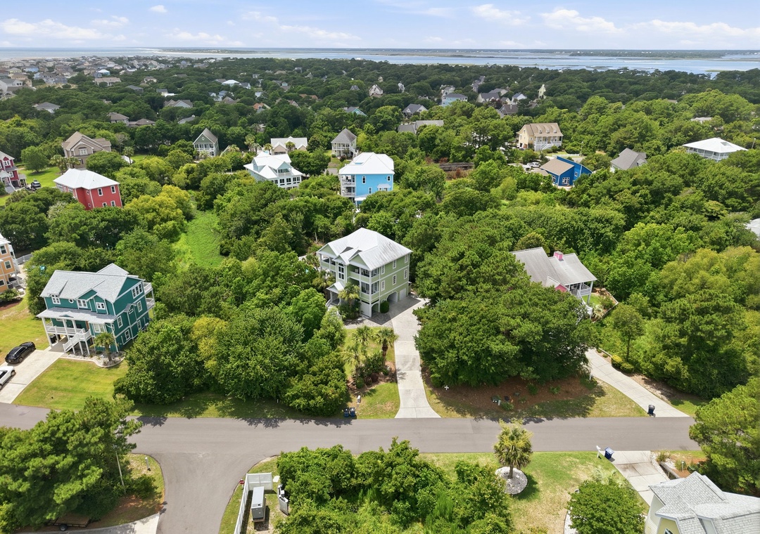 Aerial view of a coastal residential neighborhood nestled among lush trees with waterfront views, showcasing the property's peaceful location near the shore.