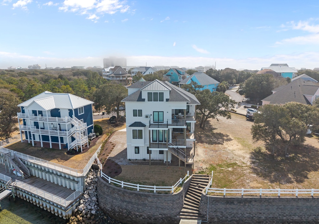 Waterfront vacation homes nestled among coastal trees with private docks and sandy paths leading to the shore.