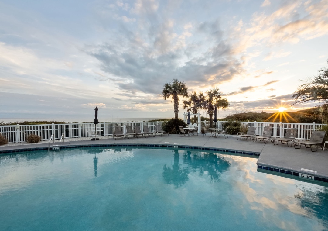 Beautiful poolside sunset with palm trees and outdoor seating creating the perfect evening atmosphere.