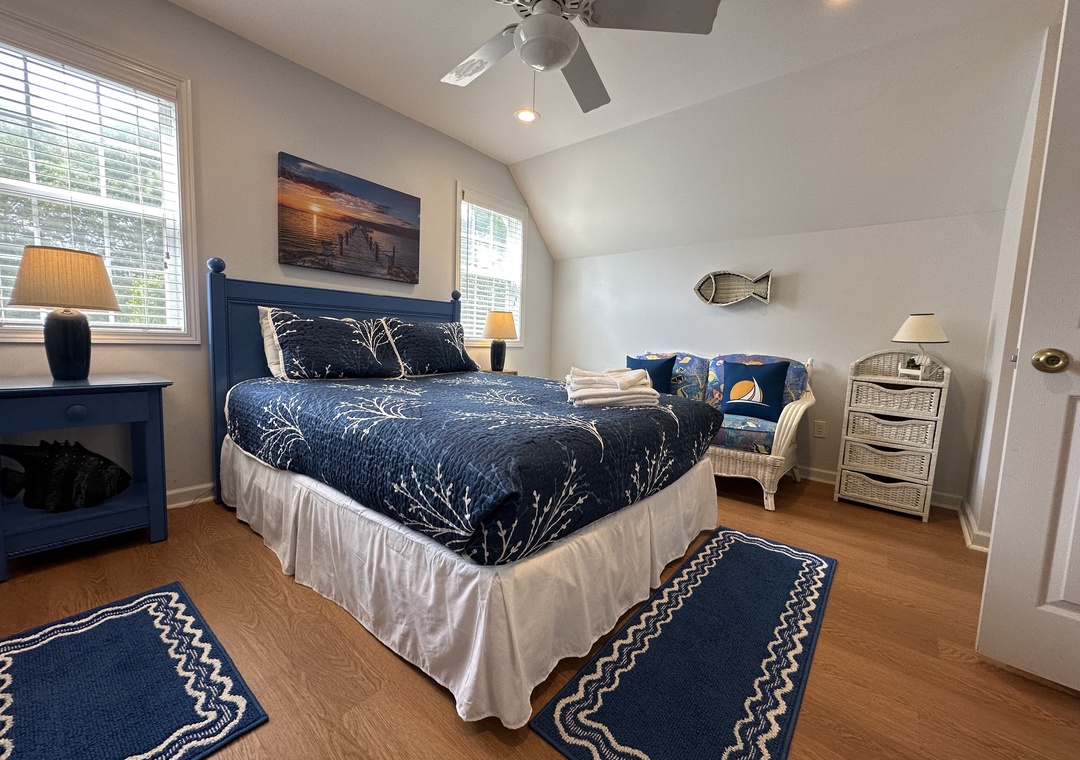Drift off in your coastal-themed bedroom, where navy hues and nautical accents create a serene retreat. A ceiling fan keeps you cool while soft lighting sets a peaceful mood.