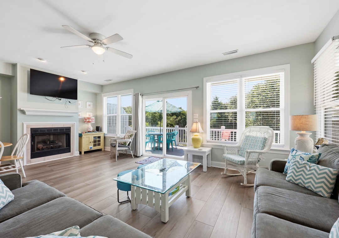 Relax in your bright, breezy living room with coastal decor, a cozy fireplace, and balcony doors opening to fresh air and views.