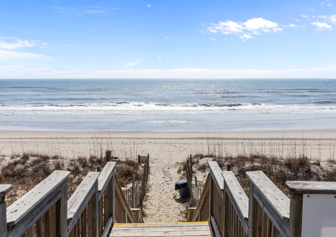 Peaceful ocean waves and sandy shores await, accessed via wooden walkway beneath clear blue skies—part of the property's coastal surroundings.