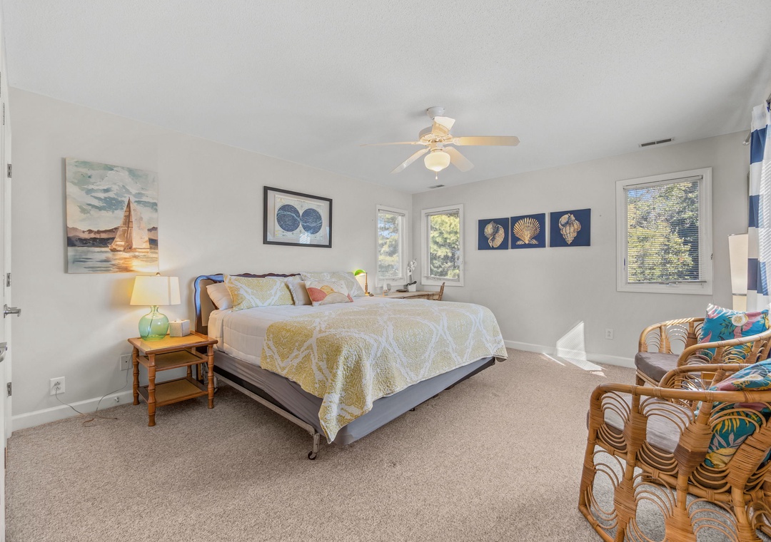 Relax in your coastal-themed bedroom with charming nautical artwork, cozy reading chairs, and gentle ceiling fan keeping you comfortable.