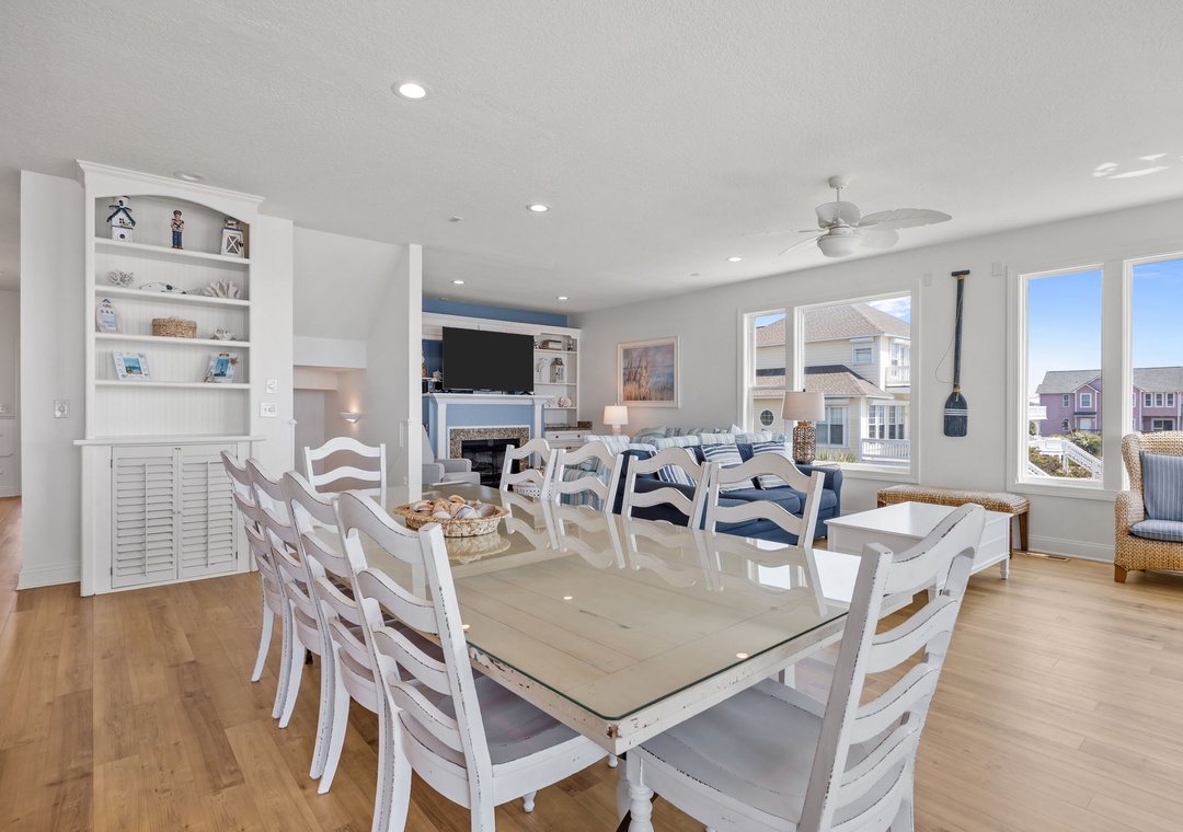 Your bright dining space flows seamlessly into the living area, where white coastal furnishings and built-in entertainment center create perfect gathering spots.