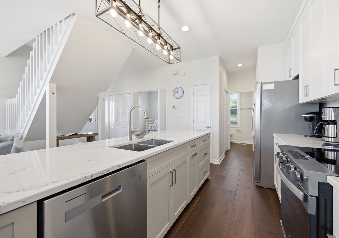 Your fully equipped kitchen features sleek white cabinetry, modern stainless appliances, and a spacious island with a farmhouse sink—perfect for preparing meals together or enjoying morning coffee.