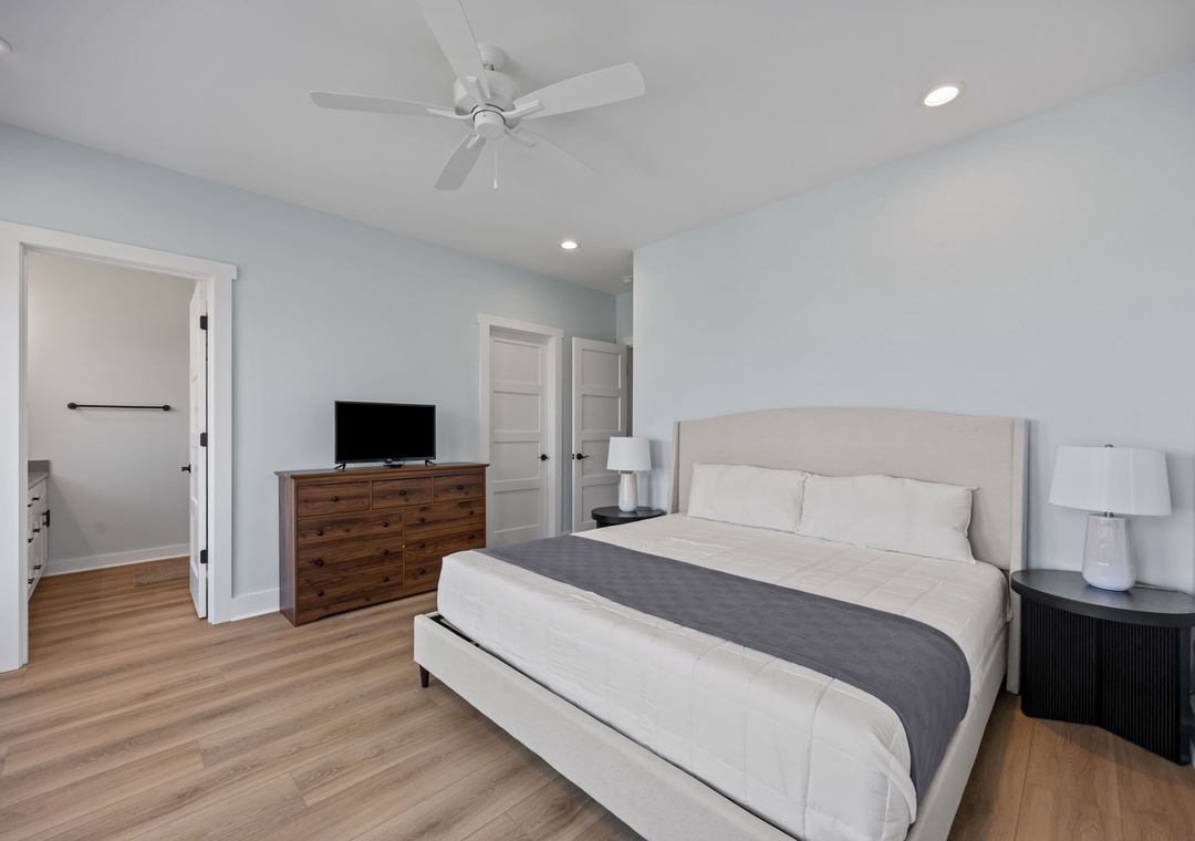 Unwind in this serene bedroom with plush bedding, modern amenities, and gentle ceiling fan for your perfect night's rest.