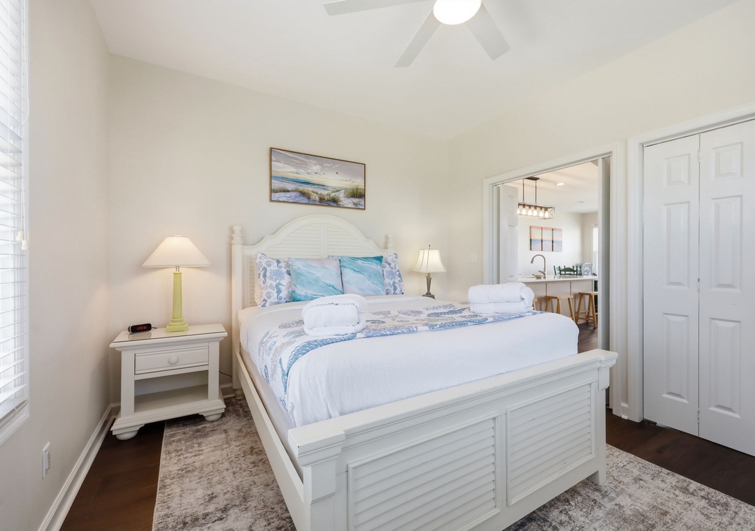 Unwind in your serene coastal-themed bedroom, featuring a plush bed dressed in soft blues and fresh linens, with airy vaulted ceilings and warm bedside lighting welcoming you home.