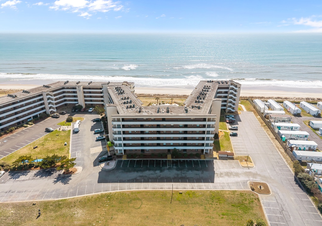Beachfront property featuring multiple buildings with direct ocean access, parking areas, and nearby accommodations along a pristine sandy shoreline under clear blue skies.