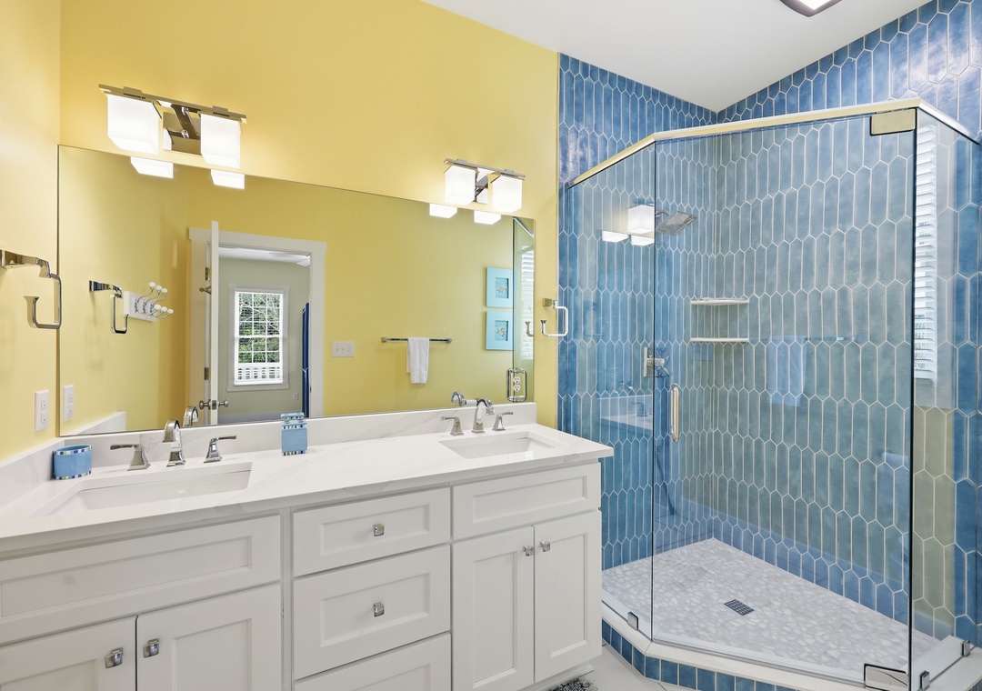 Step into your bright, modern bathroom with stunning blue hexagon tile shower, dual vanity sinks, and ample natural light streaming through the window.