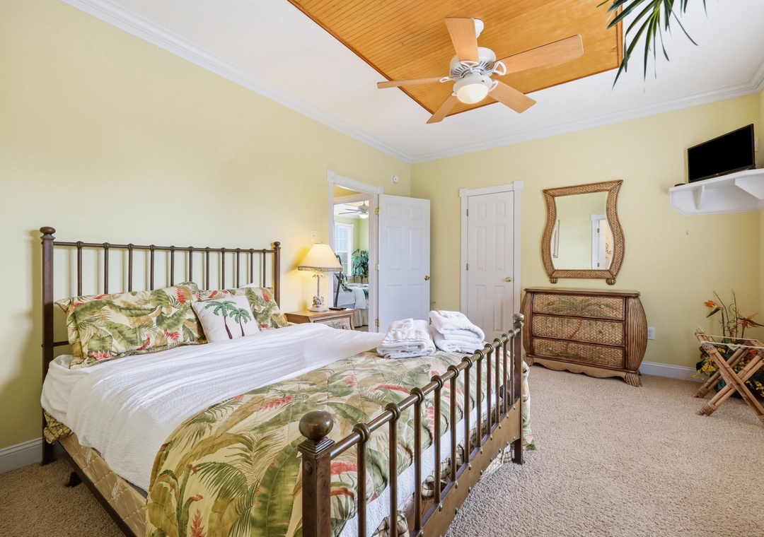 Your sunny retreat features a tropical-themed bed with lush botanical linens, a cozy tray ceiling with a fan, and island-inspired furnishings that create a peaceful, breezy atmosphere for restful nights.