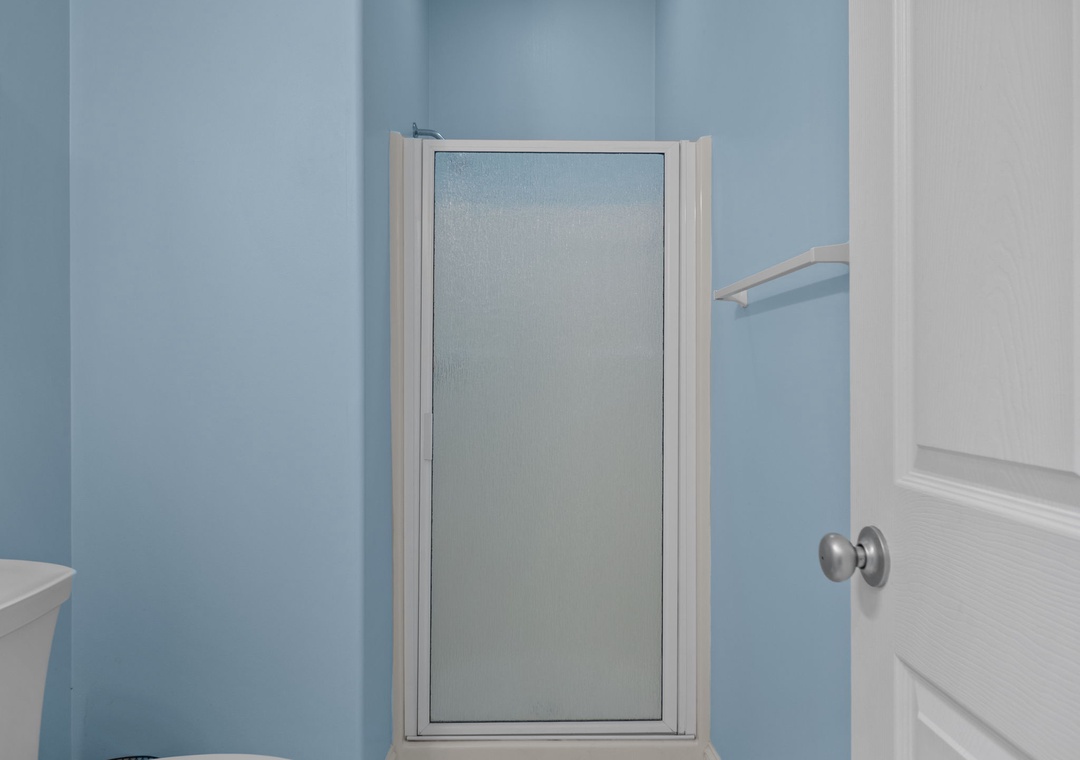 Step into your private bathroom featuring a spacious glass shower enclosure with calming blue walls that create a serene, spa-like atmosphere.
