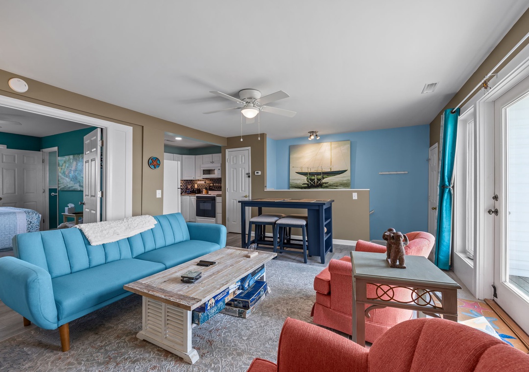 Relax in your bright, coastal-themed living space with comfortable seating, modern kitchen access, and cheerful turquoise accents throughout.